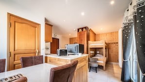 Une cuisine compacte avec des meubles en bois, un îlot central doté d’un grille-pain, un lit avec une couchette superposée et une fenêtre avec des rideaux.