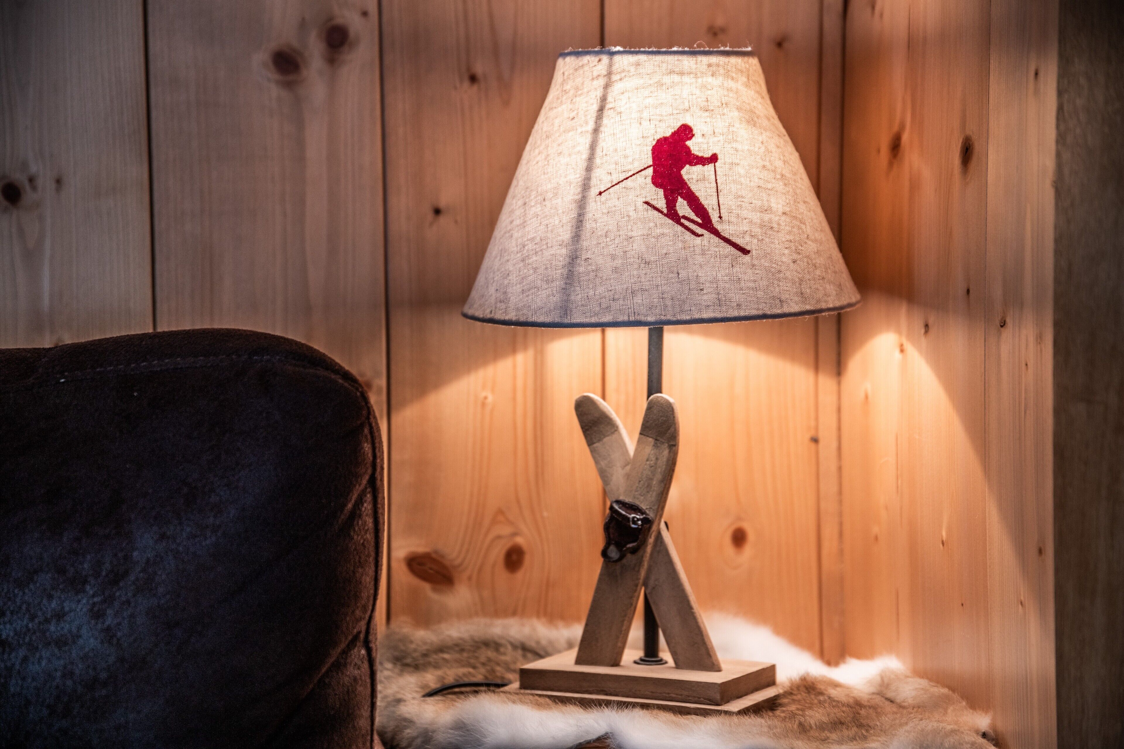 Een lamp met een silhouet van een skiër op de kap, een houten voet en een vachtkleed.