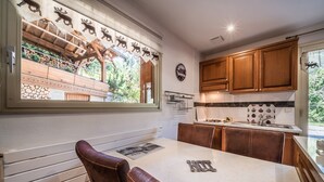 A kitchen with wooden cabinets, a marble countertop, and a window with a view of a wooden deck and greenery. - Studio 'Au Rêve Savoyard 1' with Shared Terrace, for 2 People (Morillon)