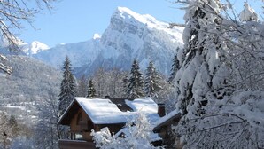 A wooden lodge with a snow-covered roof, surrounded by snow-laden trees and mountains in the background. - Studio 'Au Rêve Savoyard 1' with Shared Terrace, for 2 People (Morillon)