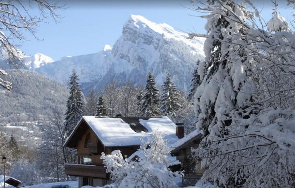 A wooden lodge with a snow-covered roof, surrounded by snow-laden trees and mountains. - Studio 'Au Rêve Savoyard 6' with Mountain View, for 4 People (Morillon)