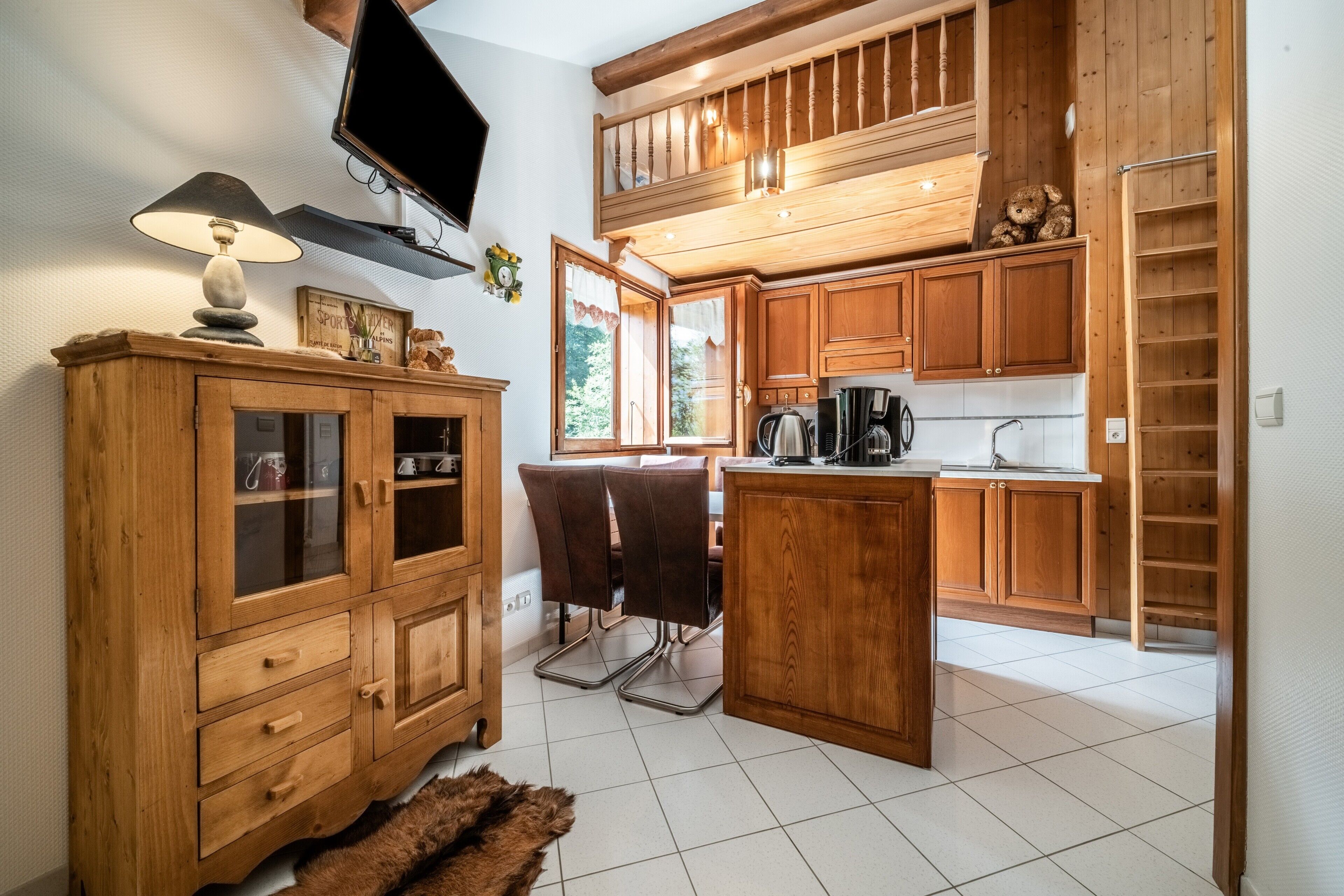 A kitchen with wooden cabinets, a dining area with chairs, a television, and a window with curtains.