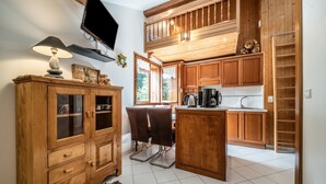 A kitchen with wooden cabinets, a dining area with chairs, a television, and a window with curtains. - Studio 'Au Rêve Savoyard 7' with Mountain View, for 4 People (Morillon)