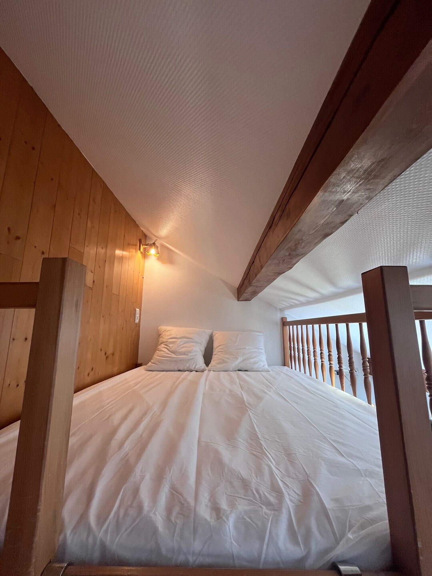 Une chambre avec un plafond en bois, un lit avec une literie blanche et une balustrade en bois.