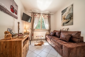 Une pièce chaleureuse avec un canapé en cuir marron, une commode en bois, un téléviseur à écran plat et une fenêtre avec des rideaux.