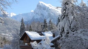 A chalet with a wooden exterior, surrounded by snow-covered trees and mountains in the background. - Apartment "Au Rêve Savoyard 5" with Mountain View for 4 People (Morillon)