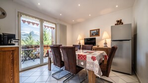 A dining area with a table set for four, a refrigerator, a television, and a view of mountains through the sliding glass door. - Apartment "Au Rêve Savoyard 5" with Mountain View for 4 People (Morillon)