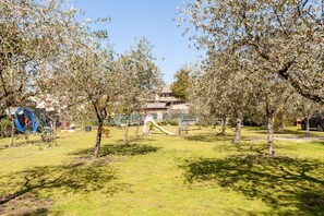 Een park met bomen, een speeltuin en een gebouw op de achtergrond.