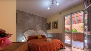 A bedroom with a bed, a nightstand, a mirror, a window with blinds, and a view of the outside. - Holiday Apartment 'Paradiso Marino' with Terrace, Garden and Wi-Fi (Cefalù)