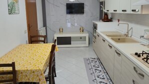 A compact kitchen with a dining table, chairs, a TV, cabinets, and a sink. - Holiday Apartment 'Paradiso Marino' with Terrace, Garden and Wi-Fi (Cefalù)