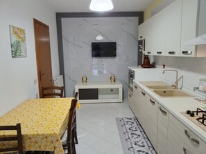 Una cucina funzionale con tavolo, sedie, televisione, pensili e lavello.