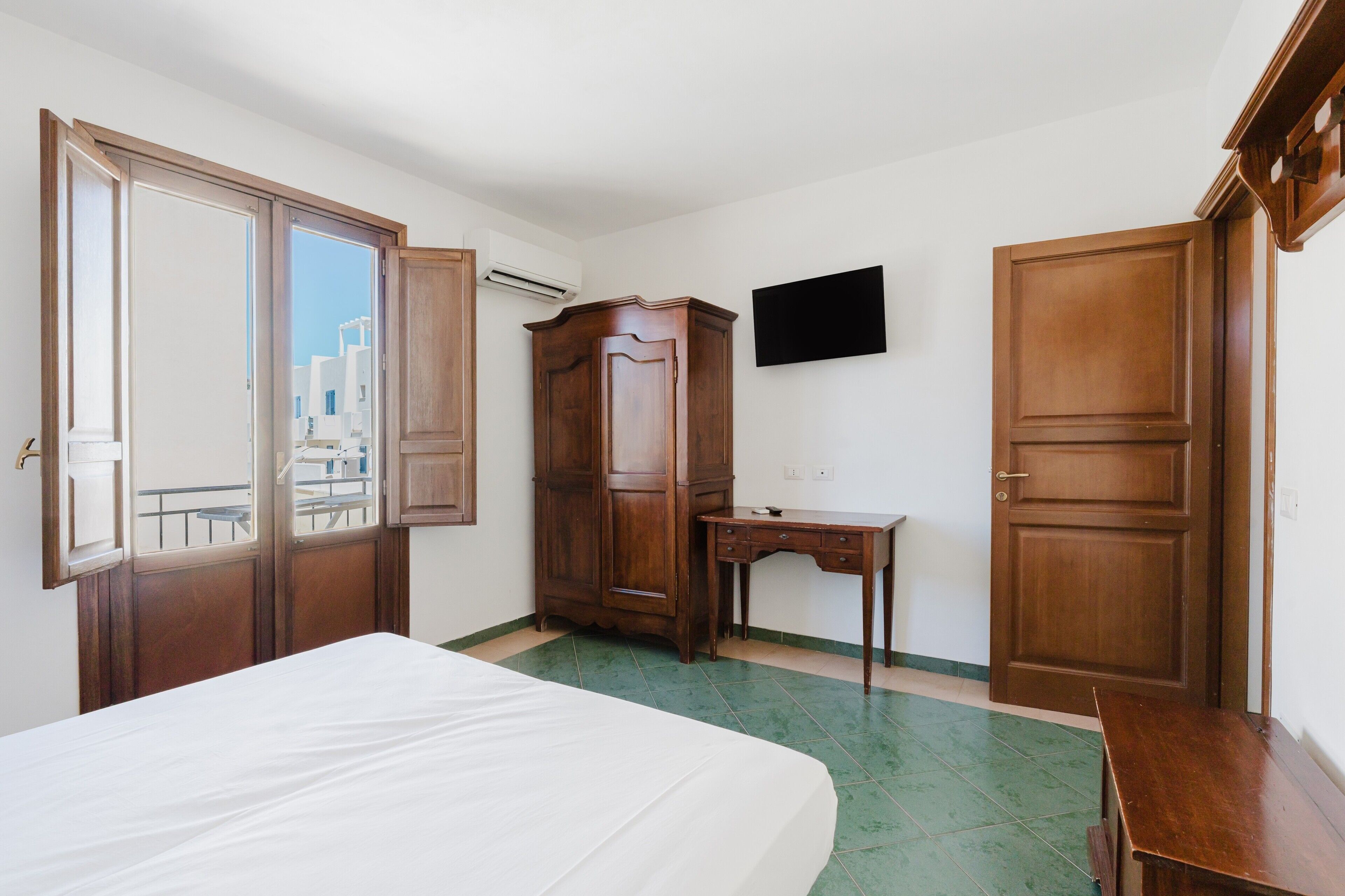 Una stanza con un letto, una scrivania, un armadio e una TV appesa al muro.