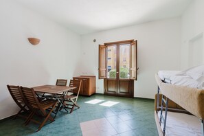 A small room with a wooden table and chairs, a bunk bed, and a window with a view of buildings.
