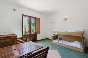 A room with a wooden table, chairs, a bunk bed, a door with a view, and a wall-mounted light fixture.