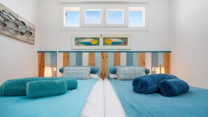 Ein Zimmer mit zwei Betten, einem hölzernen Kopfteil, einem Gemälde und einem Fenster.