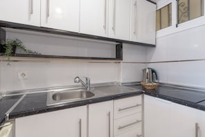 A kitchen with white cabinets, a black countertop, a stainless steel sink, and a kettle.
