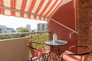 Een balkon met rieten stoelen, een glazen tafel en een lantaarn.