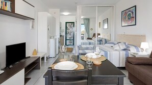 A modern living room with a TV, dining table, and a sofa. - Vacation Apartment 'Al Sole Studios Playa Roca' with Sea View, Shared Pool and Wi-Fi (Costa Teguise)
