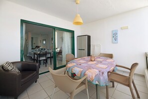 A dining area with a table, chairs, a sofa, and a sliding glass door leading to a kitchen. - Vacation Apartment 'Al Sole Studios Playa Roca' with Sea View, Shared Pool and Wi-Fi (Costa Teguise)