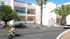 A courtyard with a palm tree, a cactus, and a building with balconies. - Vacation Apartment 'Al Sole Studios Playa Roca' with Sea View, Shared Pool and Wi-Fi (Costa Teguise)