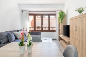 A modern living room with a sofa, a dining table with potted plants, a TV, and a wooden cabinet. - Apartment 'Can Lopits' with Balcony and Wi-Fi (L'Escala)