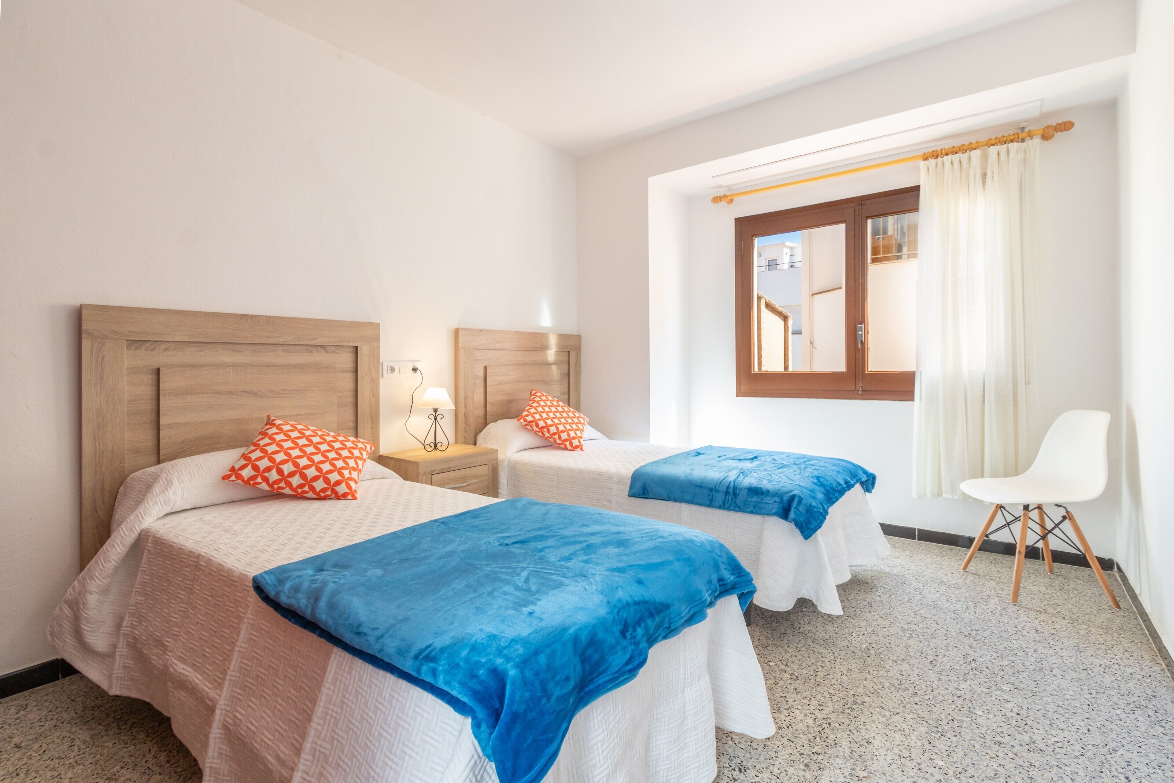 Een hotelkamer met twee bedden, een raam met gordijnen, een stoel en een nachtkastje met een lamp.