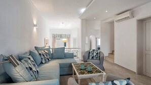 Un salon moderne avec un canapé, des fauteuils, une table basse et, au fond, un coin repas.
