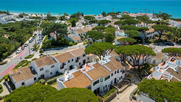Une ville côtière aux bâtiments blancs, bordée d’arbres et baignée par une mer d’un bleu limpide.