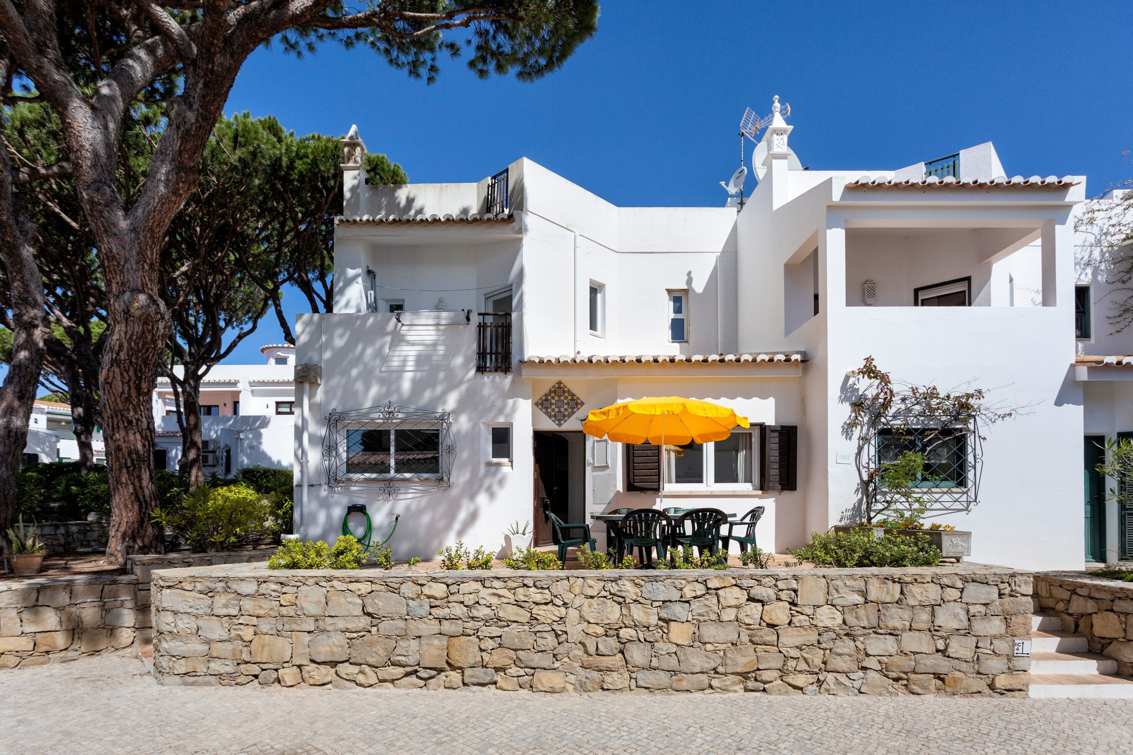 A white building with a stone wall, a yellow umbrella, and outdoor seating.