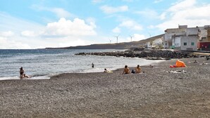 En strand med småsten, där människor sitter och det står tält, och i bakgrunden syns vindkraftverk.