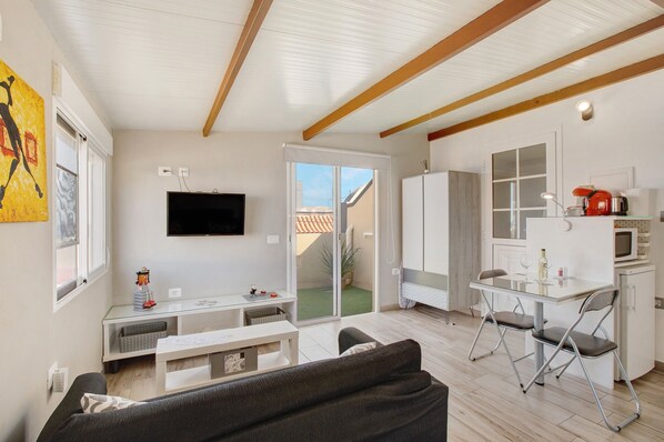 Una sala de estar moderna con sofá, televisor, mesa de comedor con sillas y una zona de cocina con microondas.