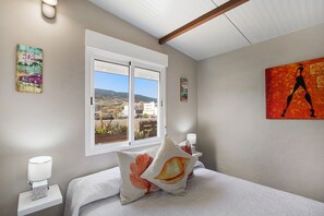 Un dormitorio con cama, almohadas, una mesita de noche, una ventana con vistas y decoración en la pared.