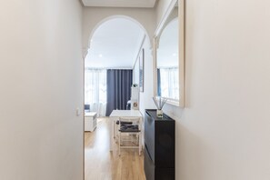 Een smalle gang die uitkomt in een eetgedeelte met een tafel, stoelen, een zwarte kast en een grote spiegel aan de muur.