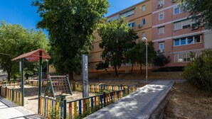 A playground with a climbing structure and a red shelter, surrounded by a colorful fence and trees.