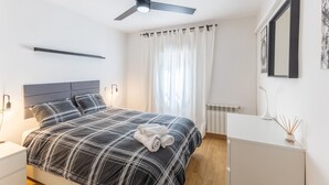A modern bedroom with a bed, bedside tables, a ceiling fan, a radiator, and a window with curtains.
