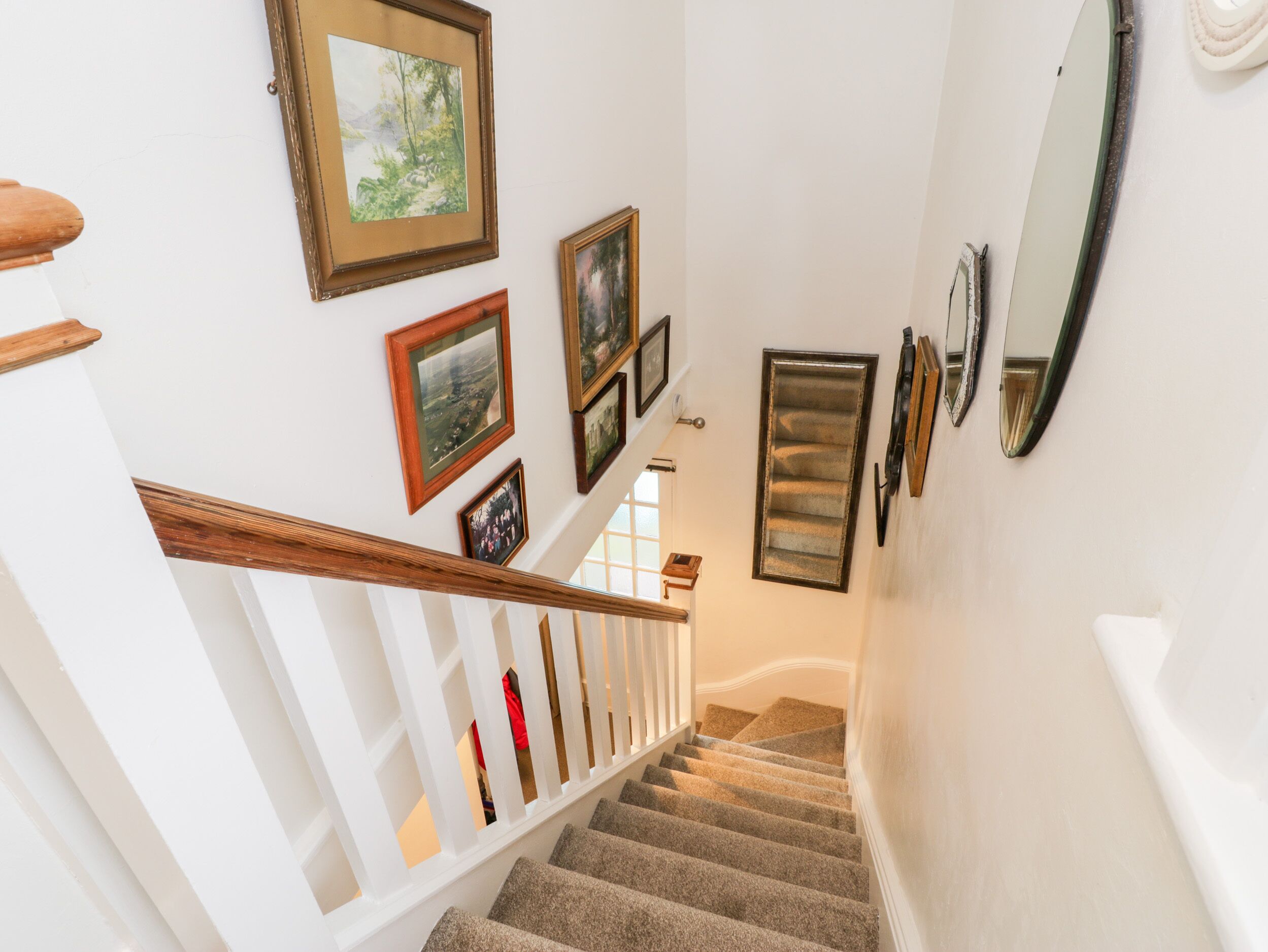 A staircase with a wooden handrail, carpeted steps, and multiple framed pictures on the walls.