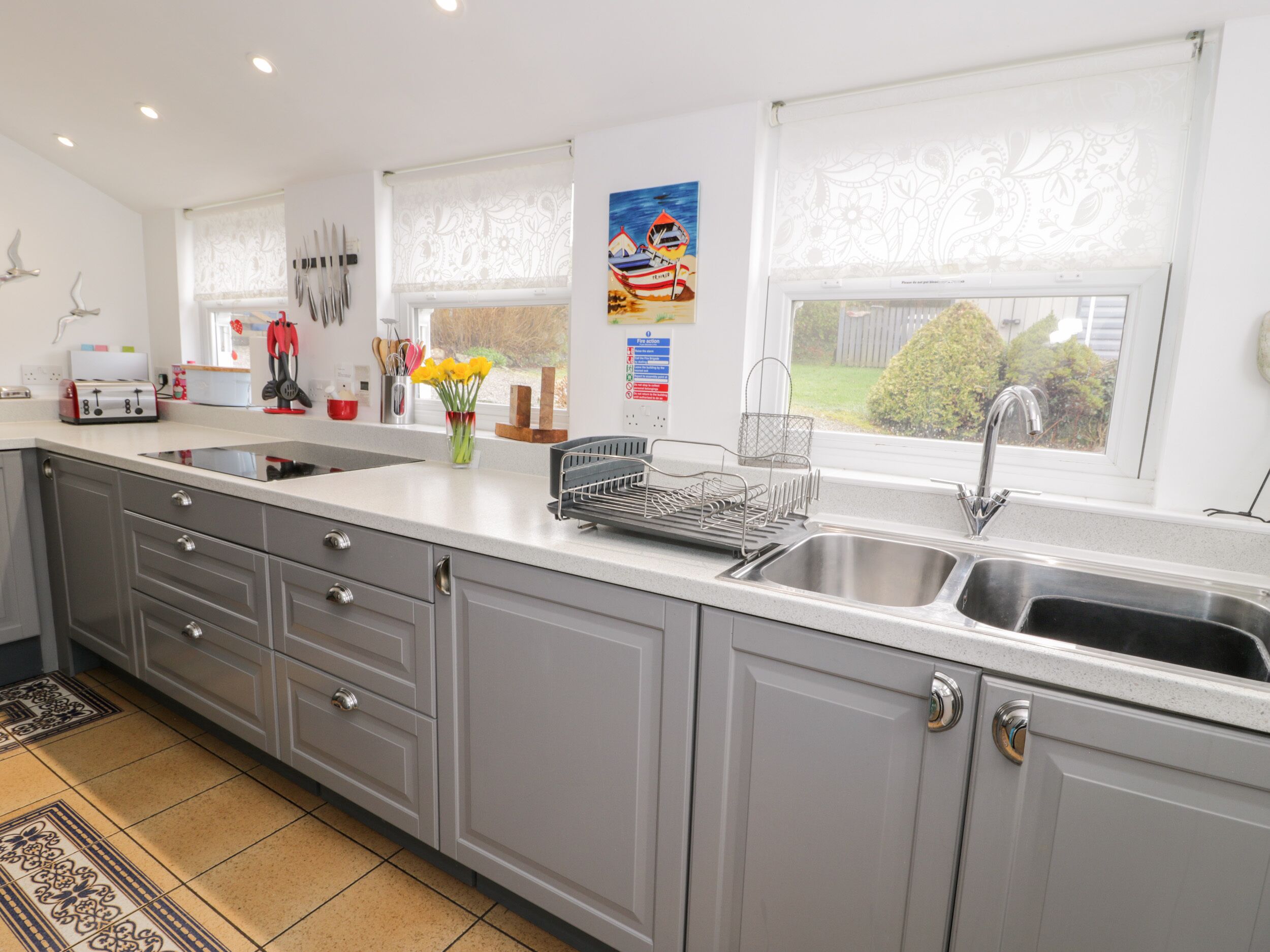 Een moderne keuken met grijze kastjes, een roestvrijstalen spoelbak en een raam met uitzicht op de omgeving.