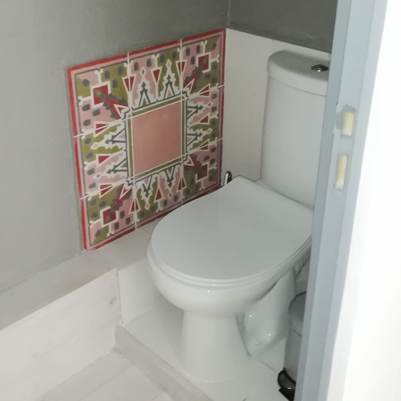 Ein Badezimmer mit einer weißen Toilette, einer Wand mit gemusterten Fliesen und einer weißen Badewanne.
