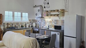 A compact kitchen with a dining area, wooden beams, a refrigerator, and a microwave. - Historic Stable House | Private Patio & Farm Views (Lagoa, São Miguel Açores)