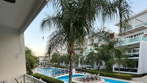 Un balcón con vista a una piscina, sillones de descanso y una palmera.