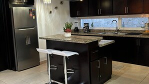 Una cocina moderna con armarios oscuros, un refrigerador de acero inoxidable, una isla integrada con taburetes de bar e iluminación colgante.