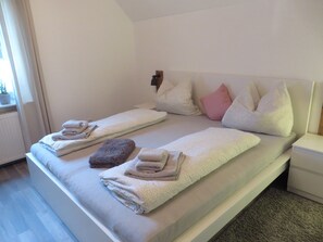 Uma cama de casal com duas almofadas, uma mesa de cabeceira e um criado-mudo.
