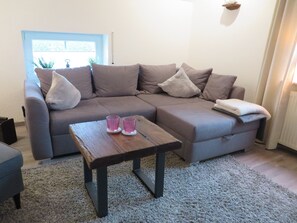 Sala de estar com um sofá cinzento, dois copos cor-de-rosa sobre uma mesa de centro de madeira e um tapete cinzento.