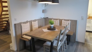 A dining area with a wooden table, cushioned benches, and pendant lighting. - Huus Inge and Manni (Dornum)