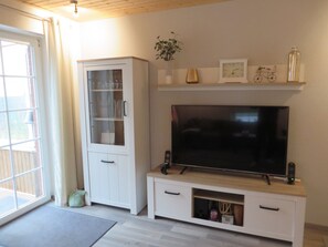 Sala de estar com televisão, armário branco e planta na parede.