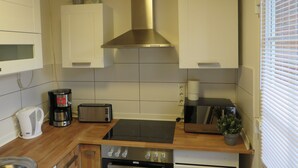 A kitchen with white cabinets, a stainless steel range hood, a toaster, a kettle, and a stove. - Huus Inge and Manni (Dornum)
