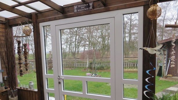 A wooden-framed door with glass panels, a hanging birdcage, and a bird feeder outside. - Huus Inge and Manni (Dornum)