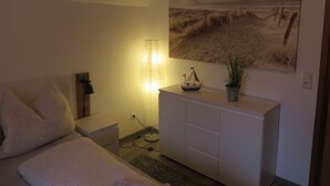 A bedroom with a bed, a bedside table, a lamp, a dresser, a painting, and a small ship model. - Huus Inge and Manni (Dornum)