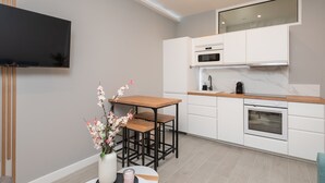 A modern kitchen with white cabinets, a wooden countertop, and a built-in oven. There is a small table with a vase of flowers and a candle. - Modern Apartment - Promenade des Anglais in Nice (Nice)