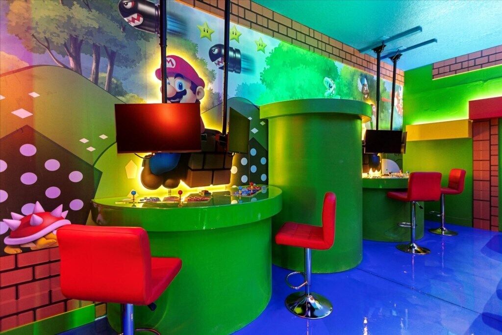 Ein hell erleuchteter Barbereich mit roten Stühlen, einer grünen Theke und einem Wandbild zum Thema Mario.